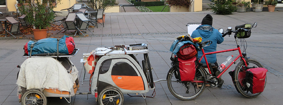 Ein wohnungsloser Mann verdient sich ein paar Euro durch Flötenspiel in einer Fussgängerzone. In seinen zwei Fahrradanhängern sind seine beiden Hunde.