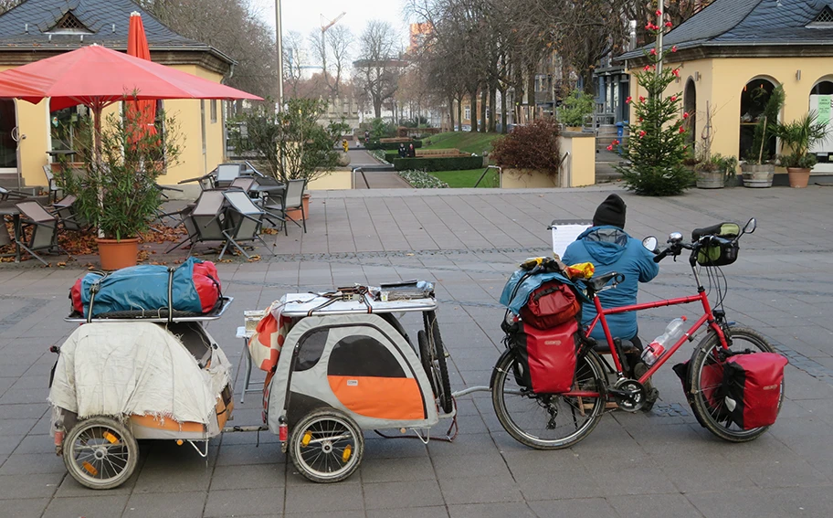 Ein wohnungsloser Mann verdient sich ein paar Euro durch Flötenspiel in einer Fussgängerzone. In seinen zwei Fahrradanhängern sind seine beiden Hunde.