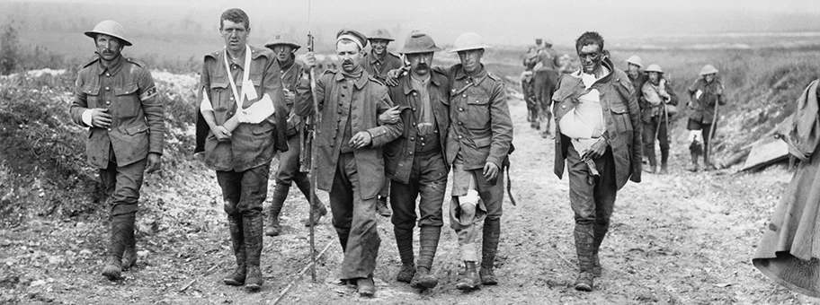 Ein deutscher Gefangener hilft britischen Verwundeten auf ihrem Weg zu einem Truppenverbandsplatz in der Nähe von Bernafay Wood nach einem Gefecht beim Höhenzug von Bazentin am 19. Juli 1916, während der Schlacht an der Somme.