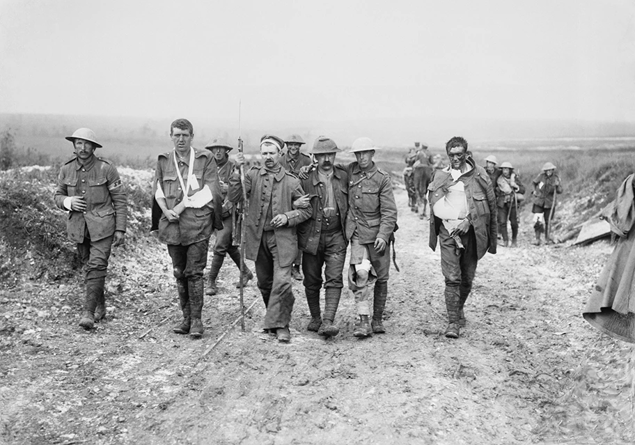 Ein deutscher Gefangener hilft britischen Verwundeten auf ihrem Weg zu einem Truppenverbandsplatz in der Nähe von Bernafay Wood nach einem Gefecht beim Höhenzug von Bazentin am 19. Juli 1916, während der Schlacht an der Somme.