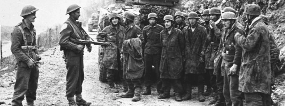 Gruppe kriegsgefangener deutscher Fallschirmjäger unter Bewachung durch neuseeländische Soldaten auf einer Strasse bei Monte Cassino, Italien, März 1944.