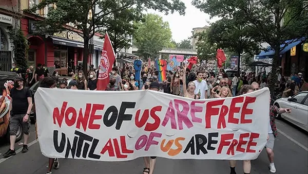 Foto vom CSD 2026 mit Transpi "None of us are free until all are free".