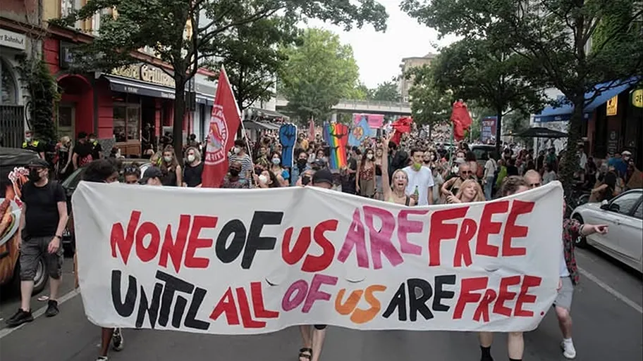 Foto vom CSD 2026 mit Transpi "None of us are free until all are free".