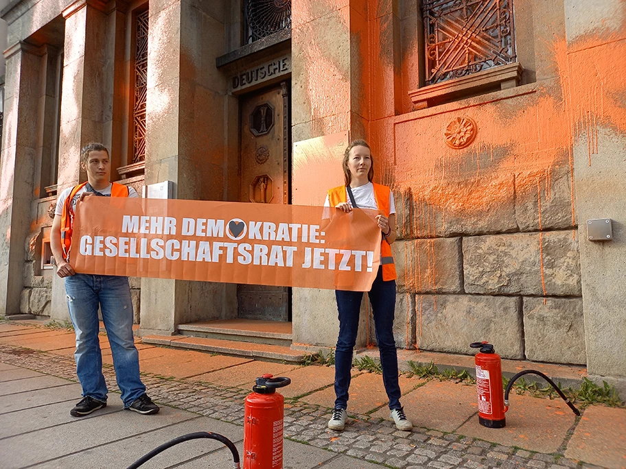 Unterstützer:innen der Letzten Generaton protestieren mit einer Farbaktion gegen die Befeuerung der Kliimakatastrophe durch die Deutsche Bank und für die Einrichtung eines Gesellschaftrats am Falkeplatz in Chemnitz.