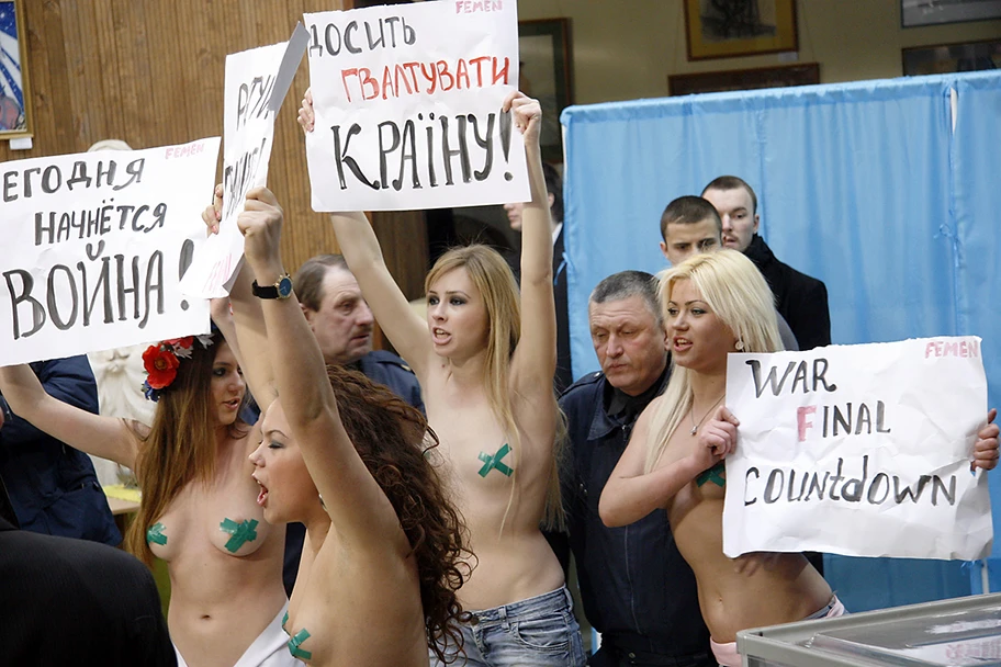 Mitglieder der Aktivistengruppe Femen protestieren am 7. Februar 2010 in einem Wahllokal in Kiew gegen das, was sie als Manipulation des demokratischen Systems ansehen. Auf den Schildern steht „Der Krieg beginnt heute“ und „Hört auf, das Land zu vergewaltigen“.