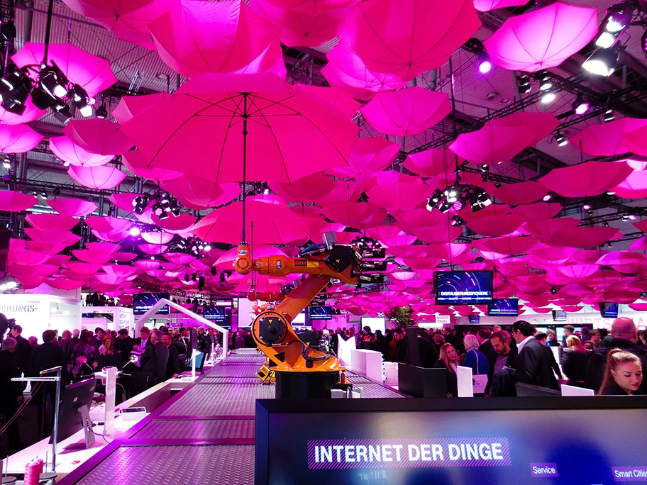 Der Messestand der Deutschen Telekom auf der CeBit 2015. Er zeigt sich bewegende Roboterarme, die magentafarbene Regenschirme halten. Das soll auf das Internet der Dinge verweisen.