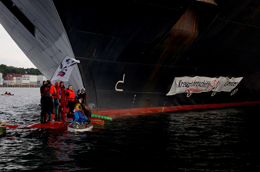 Blockade des Kreuzfahrtschiffes Zuiderdam als Protest gegen die steigenden klimaschädlichen Emissionen der Kreuzfahrtbranche, die häufig schlechten Arbeitsbedingungen an Bord und negativen ökologischen, sozialen und ökonomischen Auswirkungen auf die Zielorte des Kreuzfahrttourismus. Eine Gruppe von AktivistInnen kreuzt mit kleinen Booten vor dem Bug der Zuiderdam und ist auf den Wulstbug geklettert und verhindert so das Ablegen des Schiffes aus dem Kieler Hafen. An der Schiffswand ist ein Banner mit der Aufschrift
