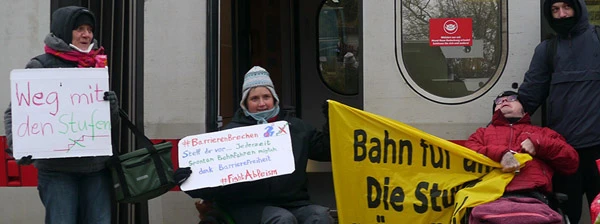 Demonstrant*innen der initiative Barrierefrei und von Rollfender Widerstand in der Tür eines ICE. Es sind nur wenige Stufen, aber mit dem Rollstuhl nicht zu überwinden.
